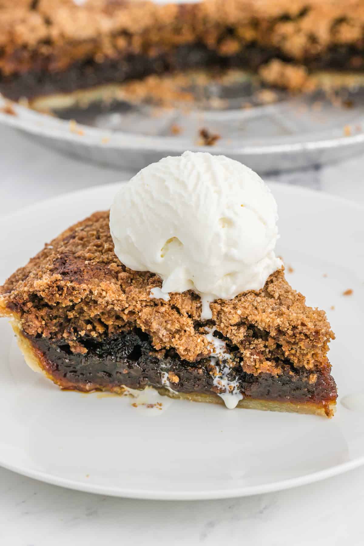 A scoop of vanilla ice cream on a slice of shoofly pie recipe on a white plate.