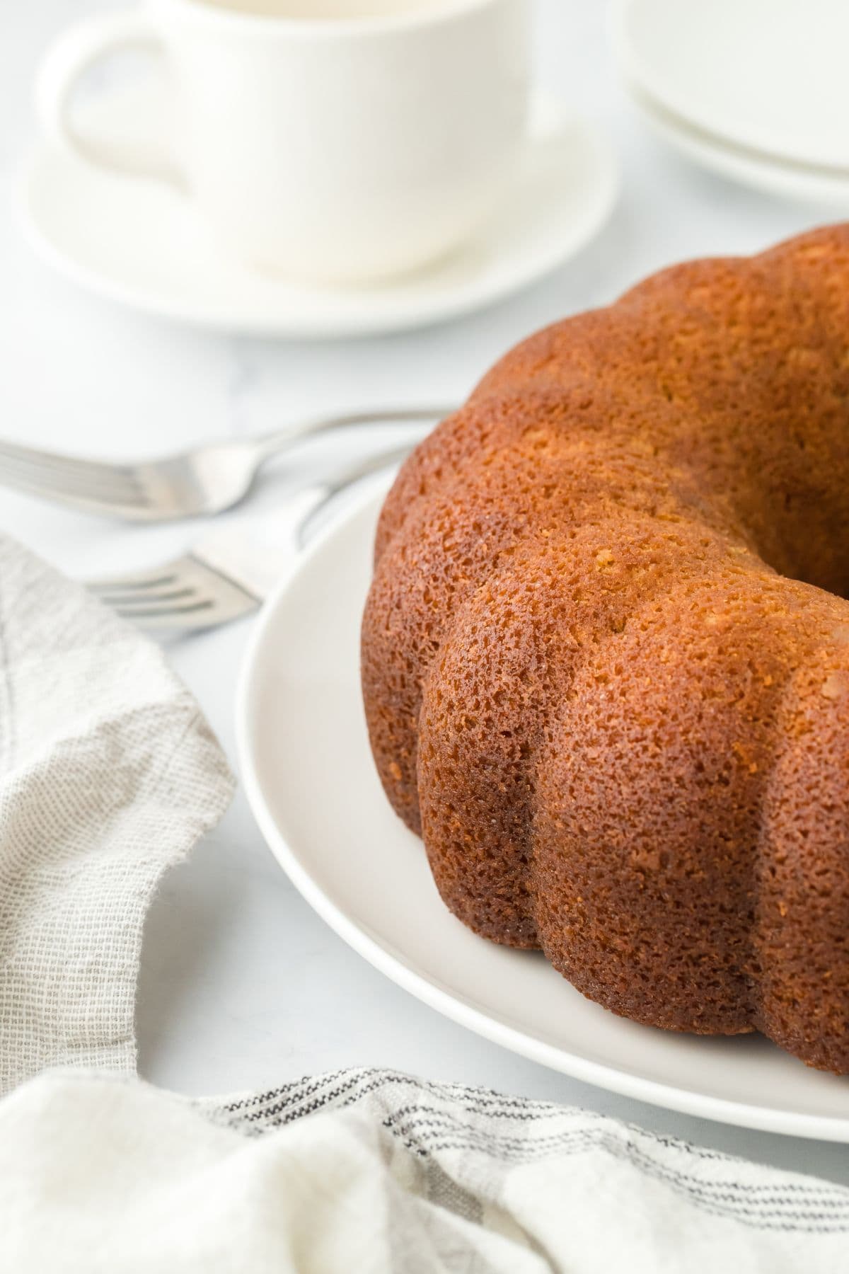 Closeup of a rum cake on a white plate with silver forks and a white mug in the background